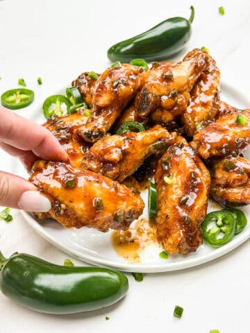 A hand grabbing a Peach Jalapeno Chicken Wing off of a plate.