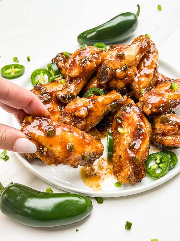 A hand grabbing a Peach Jalapeno Chicken Wing off of a plate.