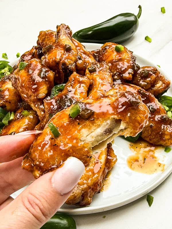 A hand holding a Peach Jalapeno Chicken Wing with a bite taken out of it.