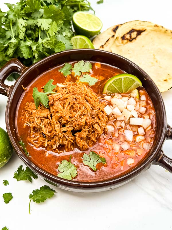 Looking down on a brown bowl full of Chicken Birria (Birria de Pollo) on a white counter.