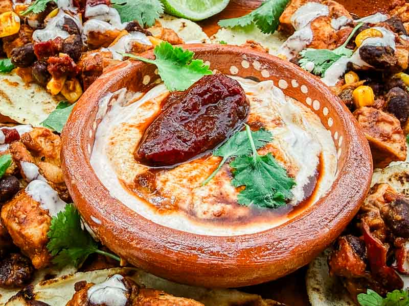 A small dish of Homemade Chipotle Crema Sauce up close with a smoked pepper on top.