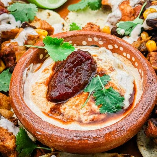 A small clay dish full of Homemade Chipotle Crema Sauce with a smoked pepper garnish.
