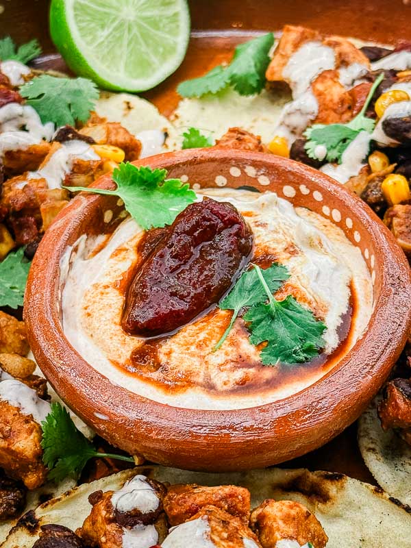 A small clay dish full of Homemade Chipotle Crema Sauce with a smoked pepper garnish.