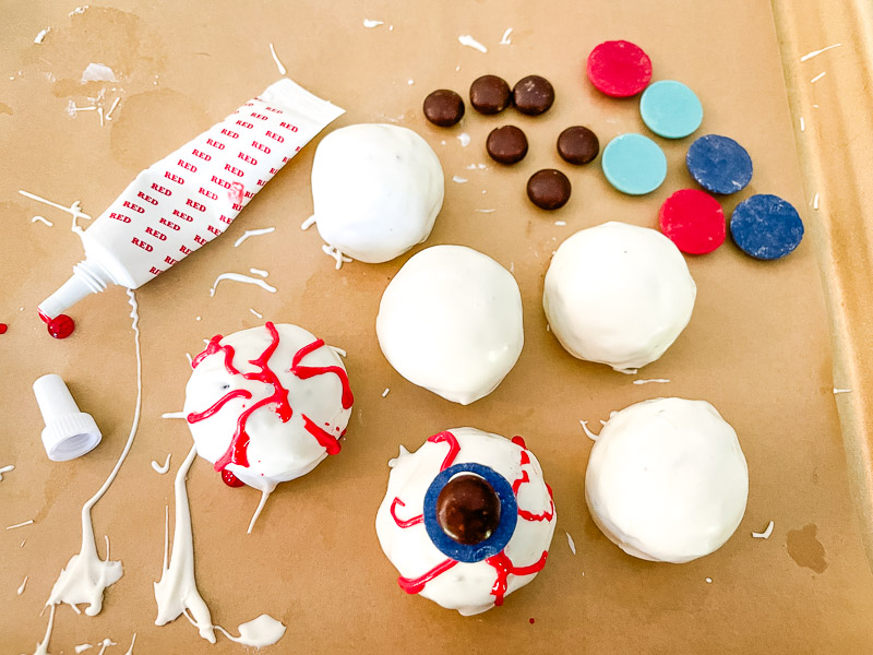 Different pieces of Halloween Eyeball Cake Pops on parchment paper during the assembly process.