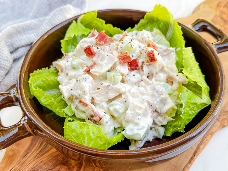 A pile of Bacon Ranch Chicken Salad sitting on lettuce leaves in a round brown bowl.