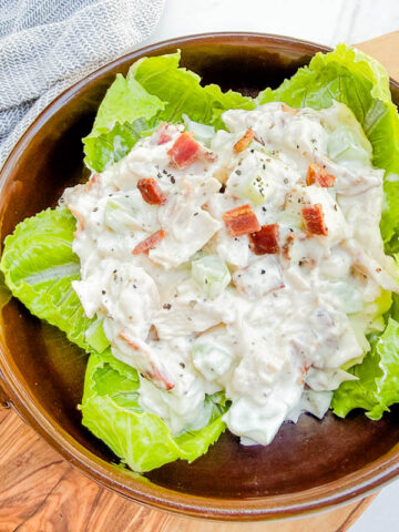 Looking down on Bacon Ranch Chicken Salad sitting on lettuce leaves in a round brown bowl.