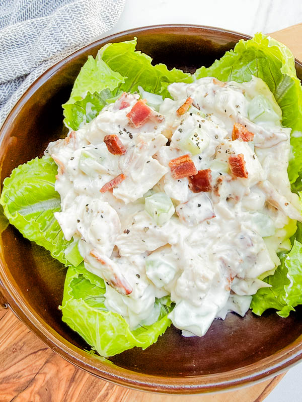 Looking down on Bacon Ranch Chicken Salad sitting on lettuce leaves in a round brown bowl.
