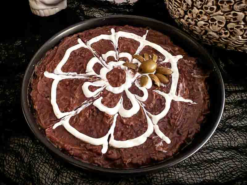 An image of the Halloween Spider Bean Dip in a dish before being eaten. A black bean dip with a white web design.