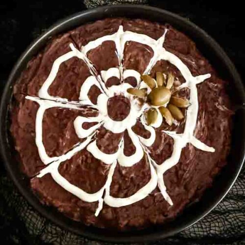 Looking down on a Halloween Spider Bean Dip with a white sour cream web design on a black bean dip and an olive spider.