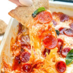 Pin of a hand dipping into Pepperoni Pizza Dip.