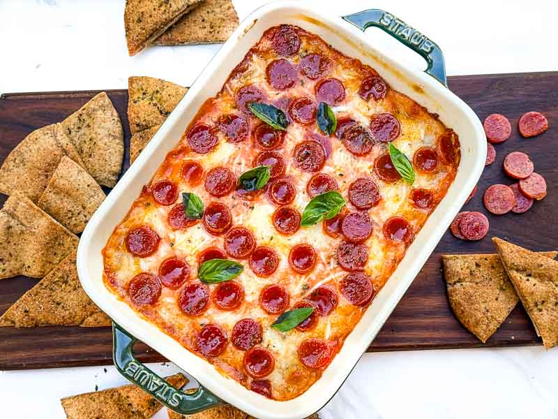 Looking down on a small rectangle dish of Pepperoni Pizza Dip sitting on a wood board.